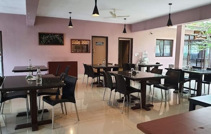 The spacious dining room at Paradise Wild Hills Resort, Kollur, with multiple tables and chairs ready for guests.