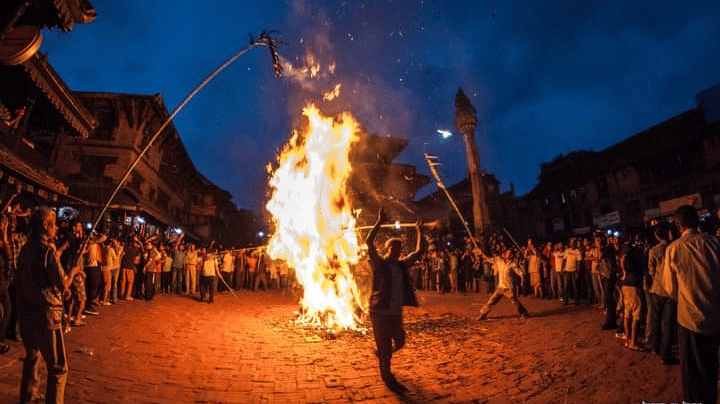 A massive bonfire illuminating a traditional stone courtyard at night during the historic Ghantakarna Chaturdashi festival in Nepal.