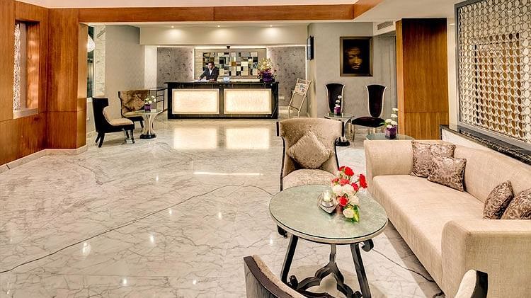 Fresh, bright lobby at HHI Select, Bangalore featuring marble floors, reception desk, cosy sofas with cushions, a coffee table with flowers, and decorative artwork on the walls.