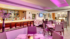 bar and restaurant with modern dining tables, cushioned chairs, a well-stocked bar, purple ambient lighting, and a mounted TV at HHI Select, Bangalore.