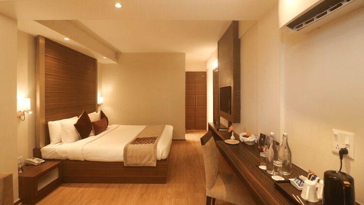 Room at Marigold Sarovar Portico, Mashobra Shimla, with a white bed, a work desk, a leather chair, warm wall lighting and polished wooden flooring nearby.