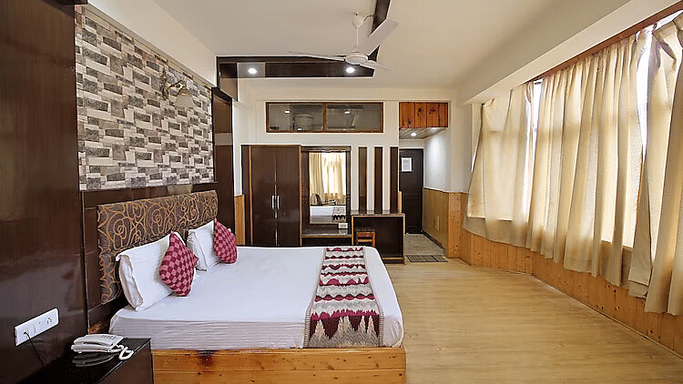 A view of a room at DLS Hotel Devlok, Manali with a double bed, side tables, a wardrobe with a mirror and  large windows