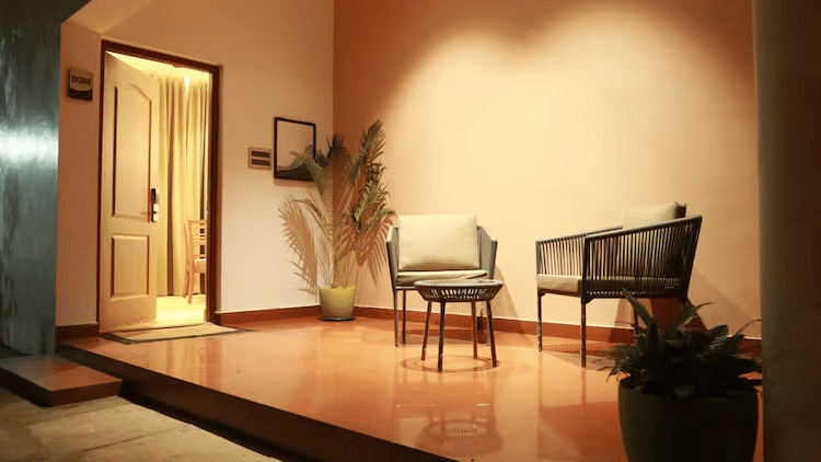 An outdoor corridor at DNC Shevaroys Resort & Spa featuring a seating area with 2 chairs, a small table, and potted plants near a doorway.