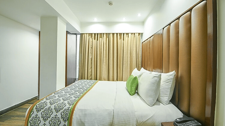 A close-up view of a comfortable king size bed with plush pillows, a textured grey runner, and soft ambient lighting - Flute Boutique By Hotel 91, Jaipur