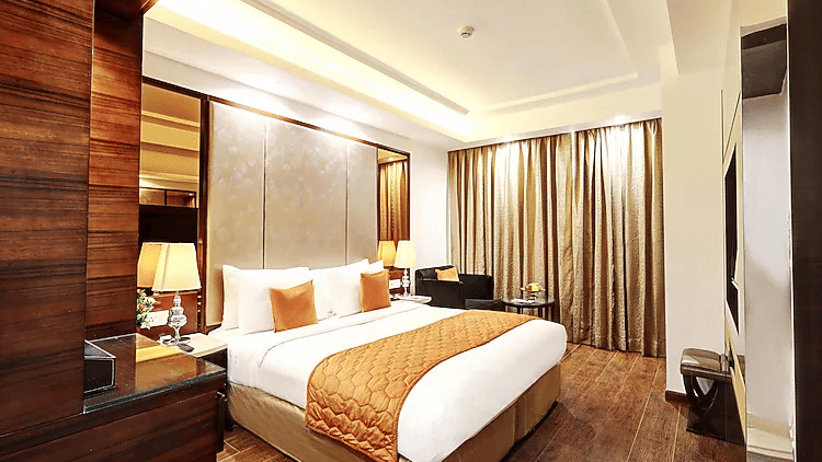 A warm and inviting guest room featuring a large bed with an orange patterned runner, wooden wall panels, and heavy gold curtains - Flute Boutique By Hotel 91, Jaipur