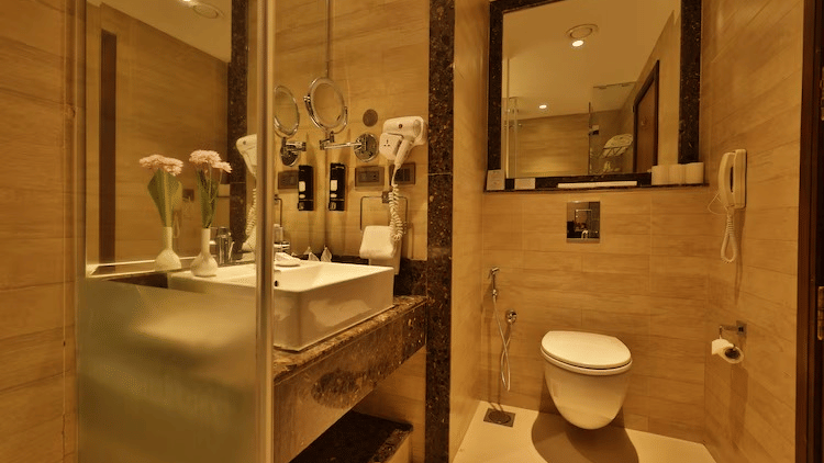 Modern bathroom at Fragrant Nature Munnar with glass shower partition, wall mounted vanity, large mirror and warm ambient lighting.