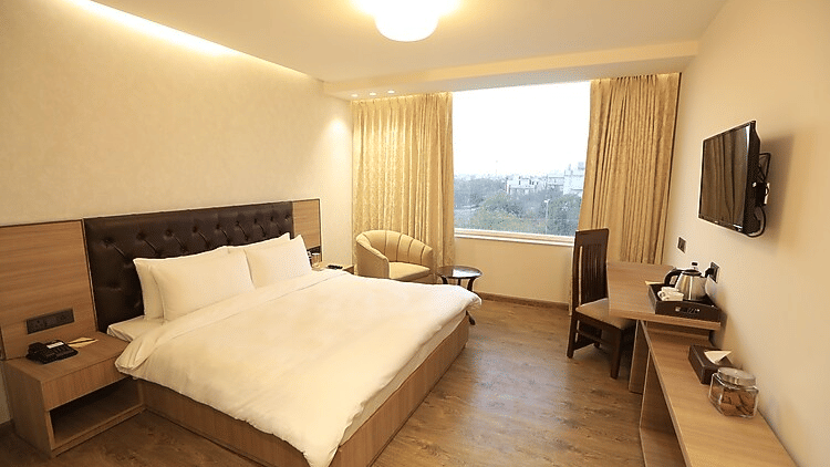 A spacious bedroom with a minimalist design, featuring a large window that lets in natural light and a dark wood headboard - Hotel 91 HUDA City Centre, Gurugram