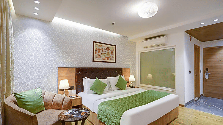 A luxury room interior showcasing a plush beige armchair with a green cushion, framed wall art, and a well-appointed bed - Hotel 91 HUDA City Centre, Gurugram