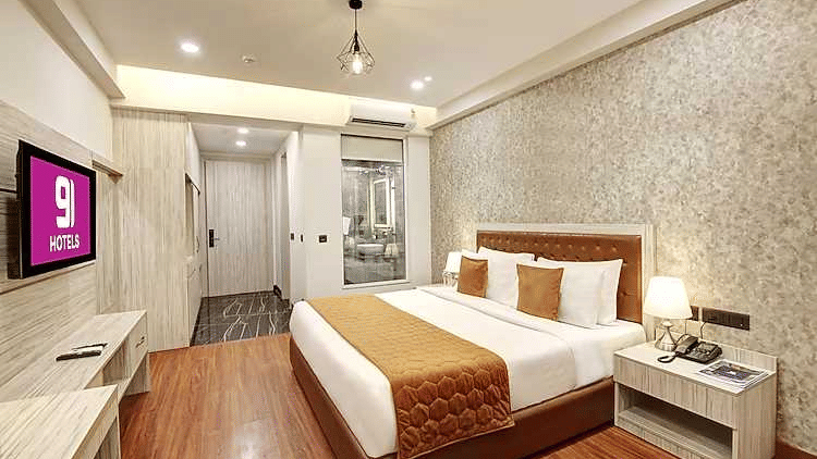 A hotel room featuring a large bed, a wall-mounted TV, a desk, and wooden flooring | Hotel 91 Millennium HUDA, Gurugram