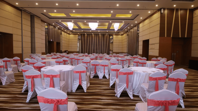 A spacious banquet hall set up for an event, featuring round tables with white and red coverings - Ramada by Wyndham Bodh Gaya Mahabodhi