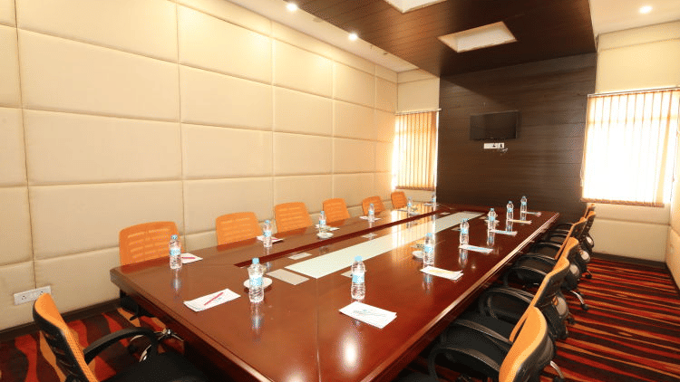 A modern, well-lit conference room with a large rectangular table and several orange chairs - Ramada by Wyndham Bodh Gaya Mahabodhi