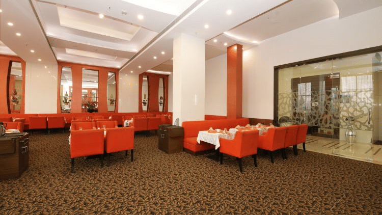 An elegant hotel dining area with several red armchairs and small tables, decorated with warm lighting - Ramada by Wyndham Bodh Gaya Mahabodhi