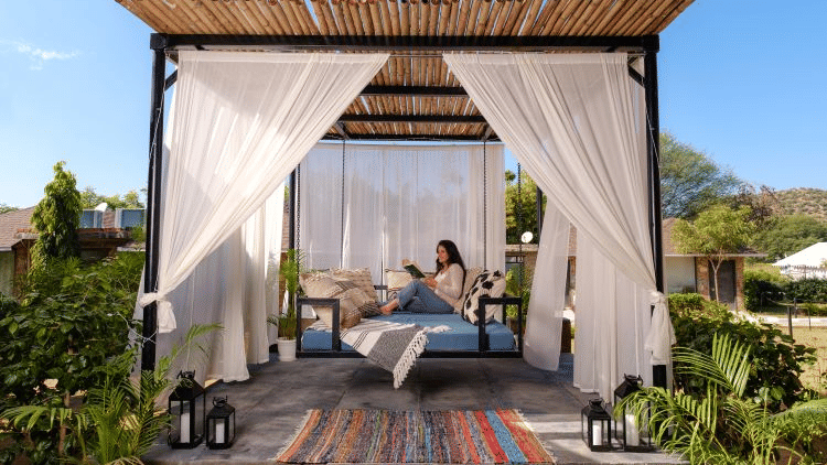 Woman reading on an outdoor sofa swing at Valley by Grassfield, a resort in Jaipur.