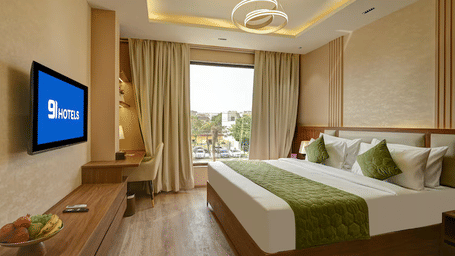 Wide-angle shot of the Executive Room featuring a double bed, a wall-mounted television, and a window with ample of natural light coming from it at Hotel 91 Privé, Gurugram.
