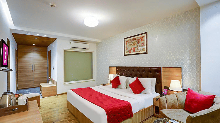 A luxury room view featuring a plush velvet armchair with red cushions, a textured feature wall, and a large bed with a matching red runner - Hotel 91 HUDA City Centre, Gurugram