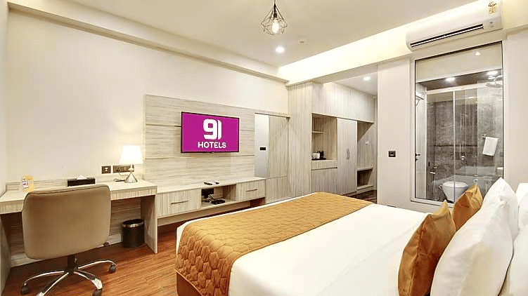 A hotel room featuring a large bed, a wall-mounted TV, a desk, and a bathroom entrance | Hotel 91 Millennium HUDA, Gurugram