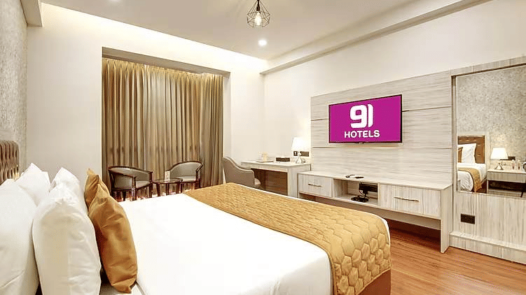 A hotel room featuring a large bed, a wall-mounted TV, a desk, and window curtains | Hotel 91 Millennium HUDA, Gurugram