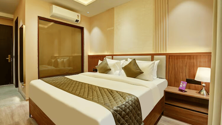 Full view of the Deluxe Room at Hotel 91 Privé, Gurugram, featuring a double bed with bed side tables on either side of it, along with a huge glass window separating the bedroom with the bathroom.