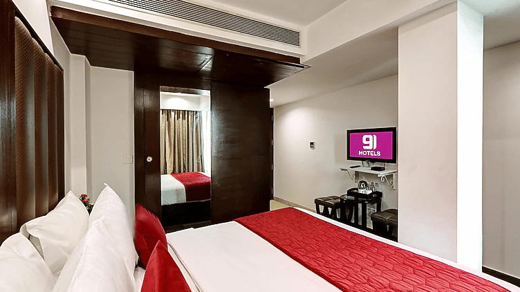 A modern hotel room with a minimalist design, featuring a bright red bed runner, white linens, and a wall-mounted television - Flute Boutique By Hotel 91, Jaipur