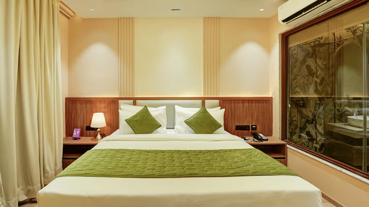 Front view of the double bed featuring a green bed runner spread on it along with cushions and pillows stacked against the headboard at Hotel 91 Privé, Gurugram.