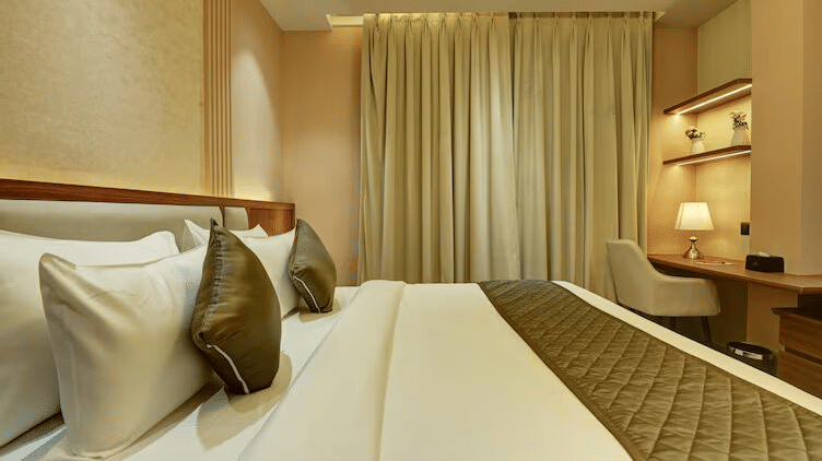 Full view of the huge double bed decorated with pillows and cushions, along with a workstation in the corner of the room at the Deluxe Room at Hotel 91 Privé, Gurugram.