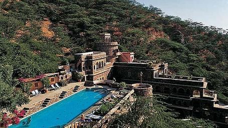 facade of neemrana fort palace in Rajasthan featuring lush greenery and a large swimming pool.
