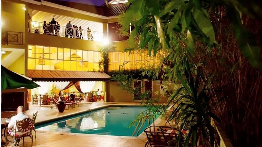 An outdoor view of a hotel at night, featuring a swimming pool surrounded by palm trees and illuminated buildings | Altamont Court, Jamaica