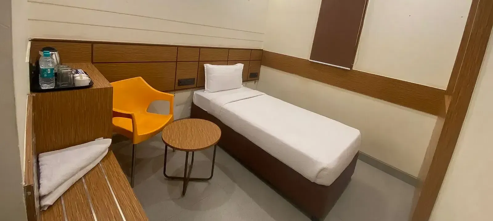 View of a hotel room with a single bed, wooden accents, and warm lighting - Max Hotel Prayagraj