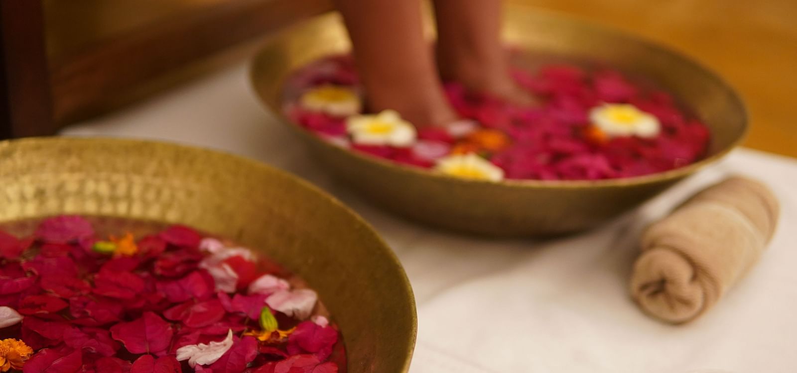 A person with their legs in a brass plate with water having rose petals