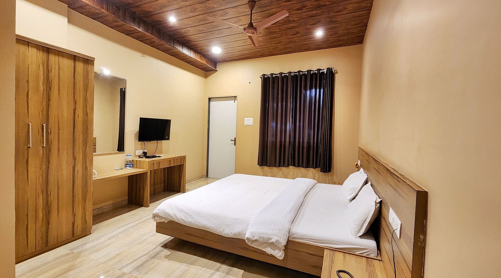 Overview of a Pool View Standard Room at The Kanila Resort with a queen sized bed, a nightstand, a TV, and a desk. 