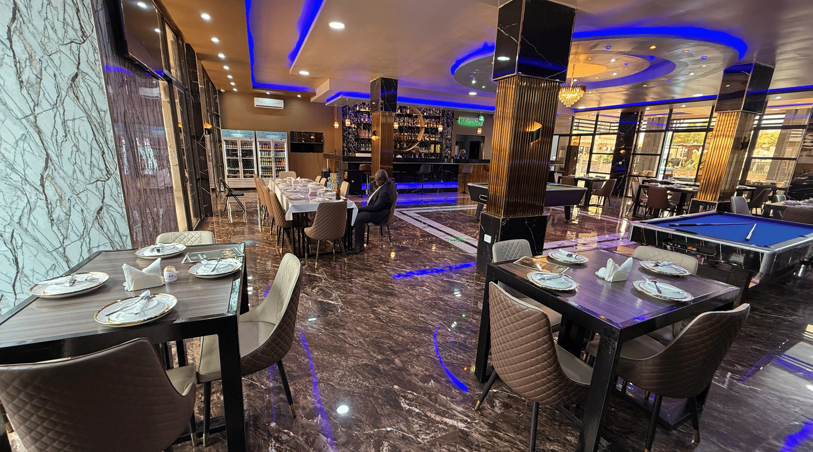 A lavish indoor dining area with marble-effect flooring, dark tables, place settings, and striking blue neon lighting at Luffu Club.