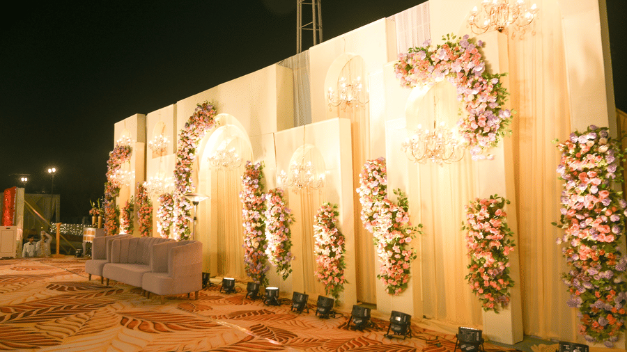 An outdoor decorative wall with arched panels, floral arrangements, and patterned flooring placed in front.