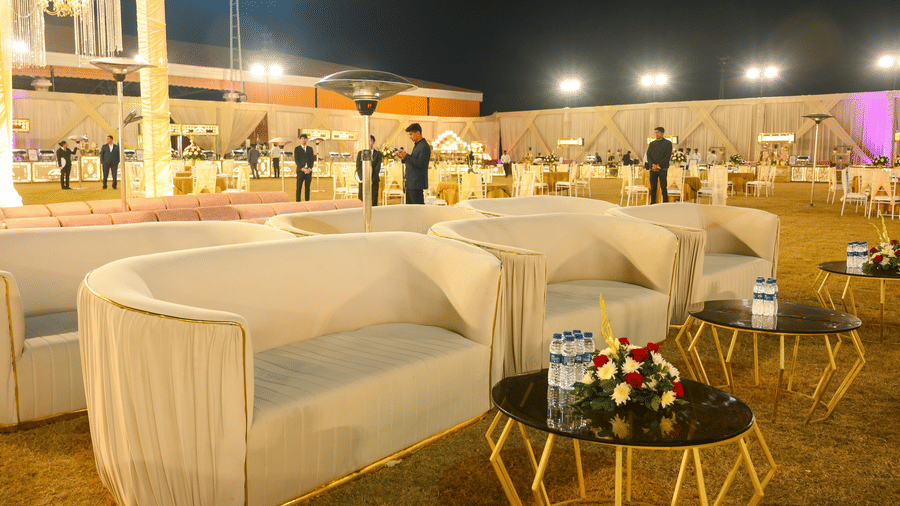 An outdoor lounge setup with sofa seating, round tables, floral centrepieces, and open event space around.