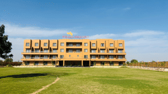 Pride Resort, Jodhpur, with a large lawn in front and a clear sky above, showcasing its modern architecture.