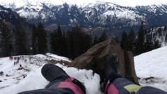 Person Wearing Black Boots and sitting in a Snowy Mountain watching a snow-capped mountain.