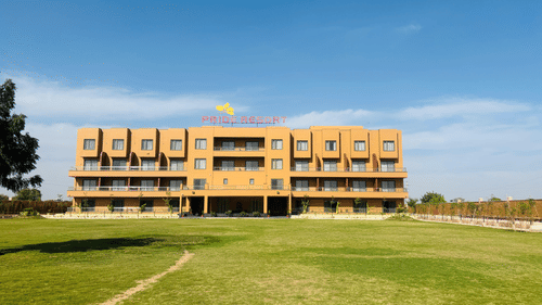 Pride Resort, Jodhpur, with a large lawn in front and a clear sky above, showcasing its modern architecture.