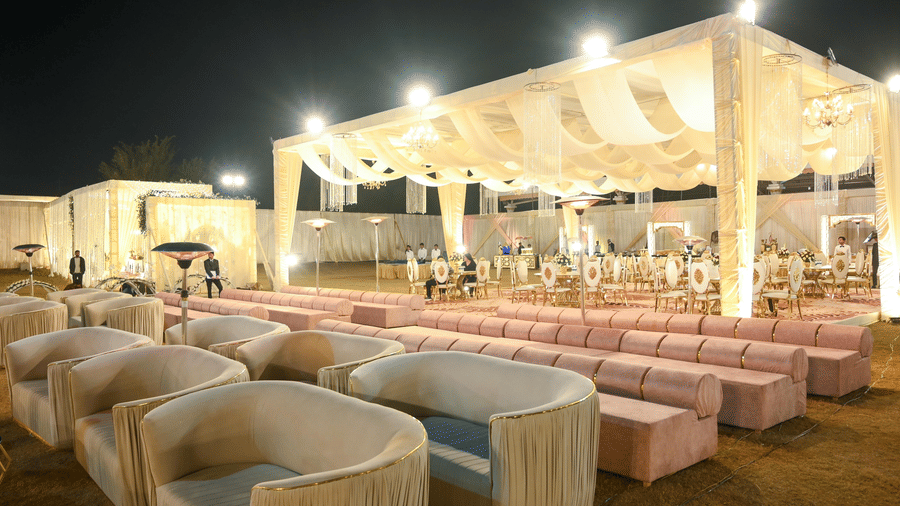 An outdoor seating arrangement with sofa blocks, low tables, and a pavilion structure with draped roofing behind.