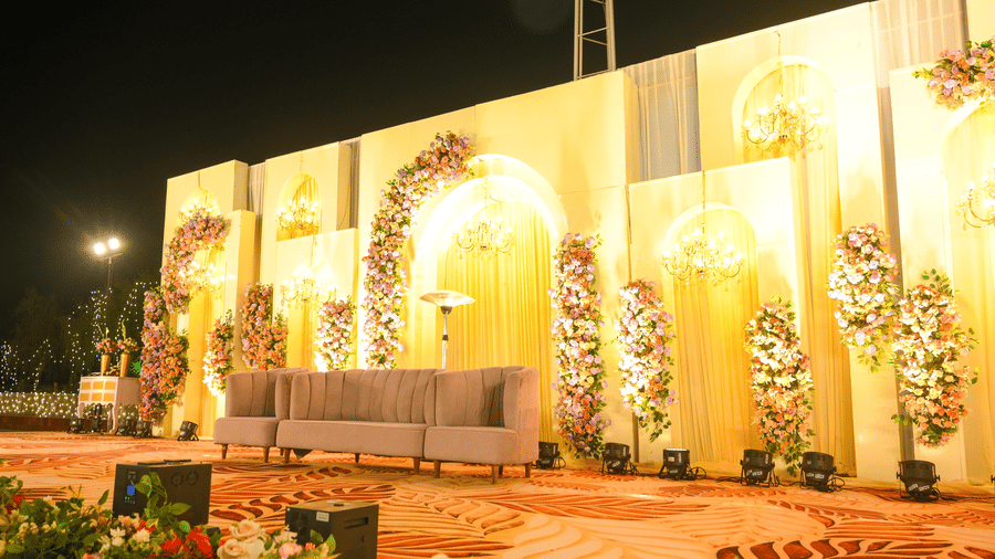 A decorative event facade with arched panels, floral arrangements, raised seating, and patterned flooring in front.
