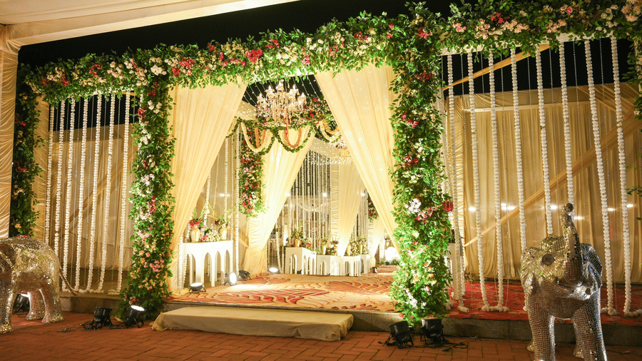 An outdoor ceremonial stage framed with floral garlands, hanging decor, seating platforms, and side drapes.
