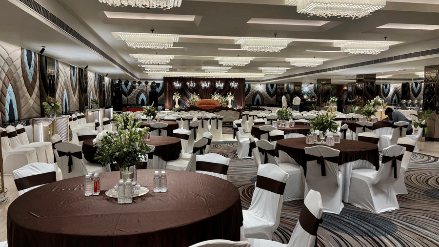 Elegantly decorated banquet hall at The Piccadily with dark wood round tables, white chair covers, floral centerpieces, and warm chandelier lighting.