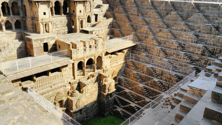 An ancient Indian stepwell, Chand Baori, featuring a massive, symmetrical network of stone steps leading to green water.