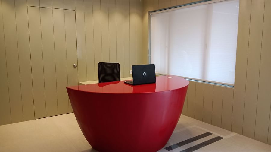 A close up view of a modern office space with a red half-oval desk and a black office chair in front of a closed window with blinds - Hotel Langford Keys by TGI, Shanti Nagar