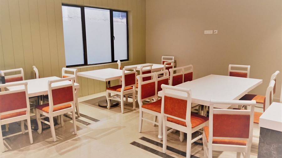 A cafeteria with white tables and chairs with orange cushions, set against a window and beige walls - Hotel Langford Keys by TGI, Shanti Nagar