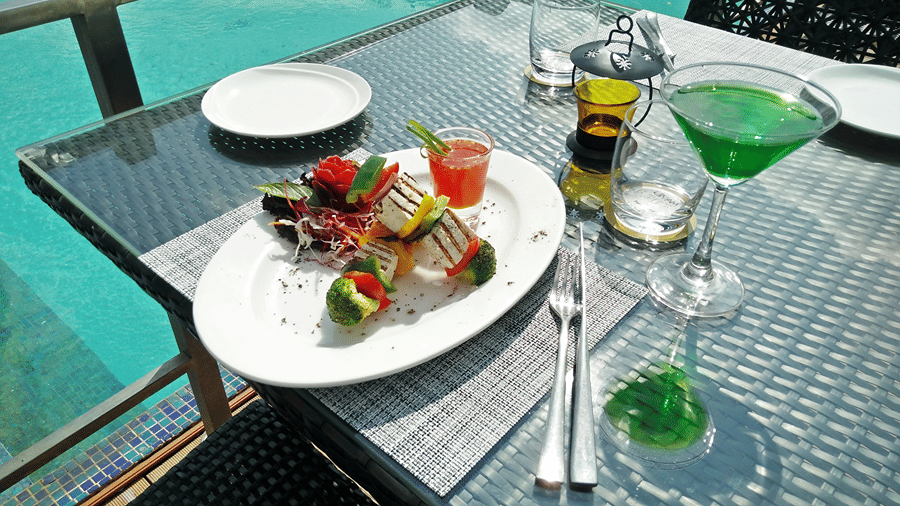 A close up shot of a delicious Indian starter topped with thinly sliced salad along with a green coloured cocktail in a martini glass - Senses Hotel
