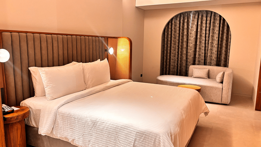 A bedroom at Swosti Premium Beach Resorts, Puri, with a made bed and an arched doorway leading to another room.