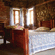 A rustic bedroom featuring a wooden bed frame, patterned blue coverlet, stone and brick walls, and sunlight filtering through windows.