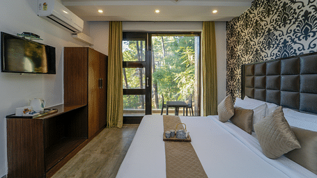 The deluxe room with a bed, a flat screen TV, an air-conditioner, and the glass door leading to the balcony with forest view - DLS Whispering Winds