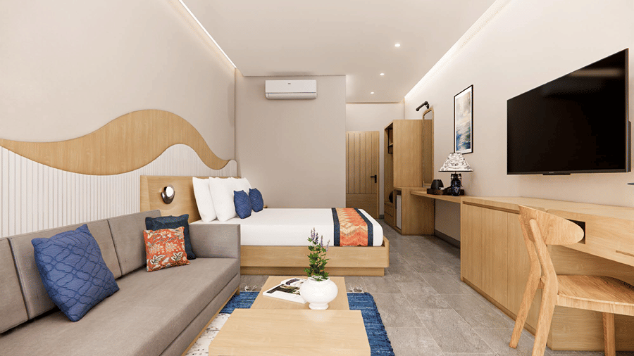 Spacious hotel guest room featuring a king bed, grey sofa seating area with a blue accent rug, wall-mounted TV, and wooden desk.