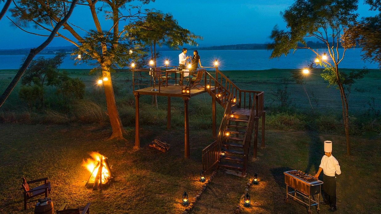 An overview of a table for two with fire lighting the ambience during twilight for a Romantic Dinner at The Serai, Kabini.