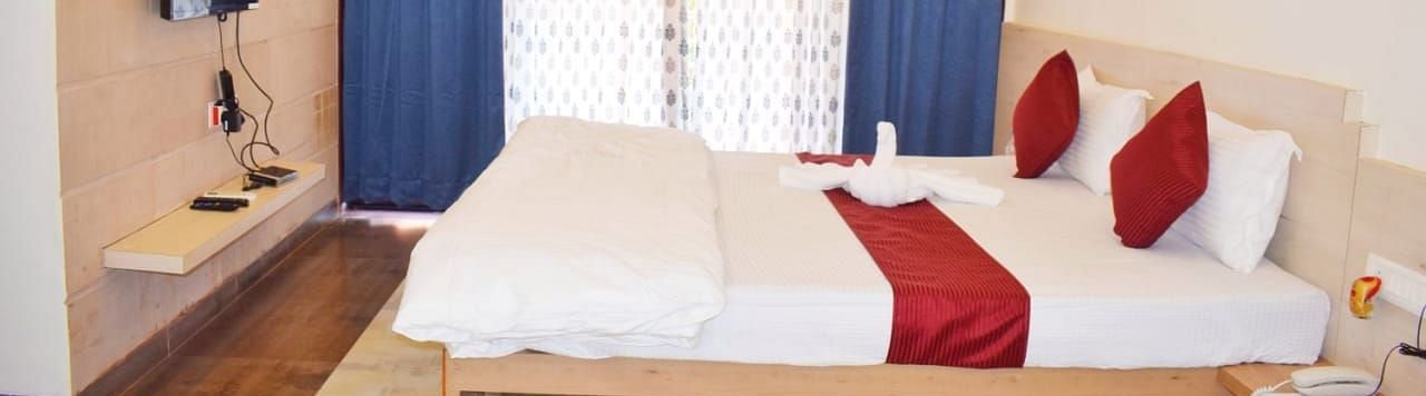 A side view of a spacious room with a large bed. Right opposite to it, there is a wall-mounted TV, and a large window with curtains fully covering it at SeaFort Beach Resort